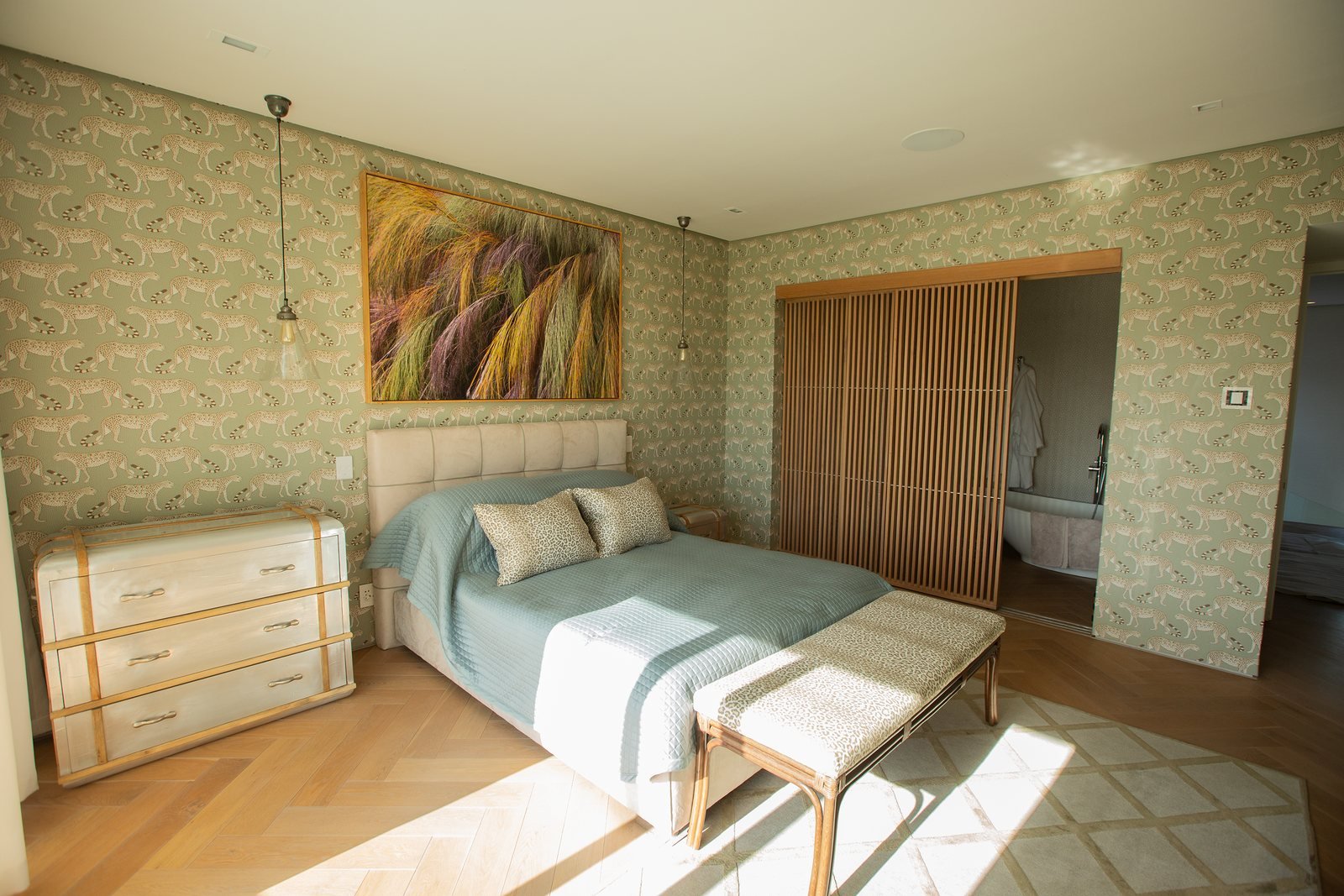 A large painting above the bed in a bedroom with patterned wallpaper