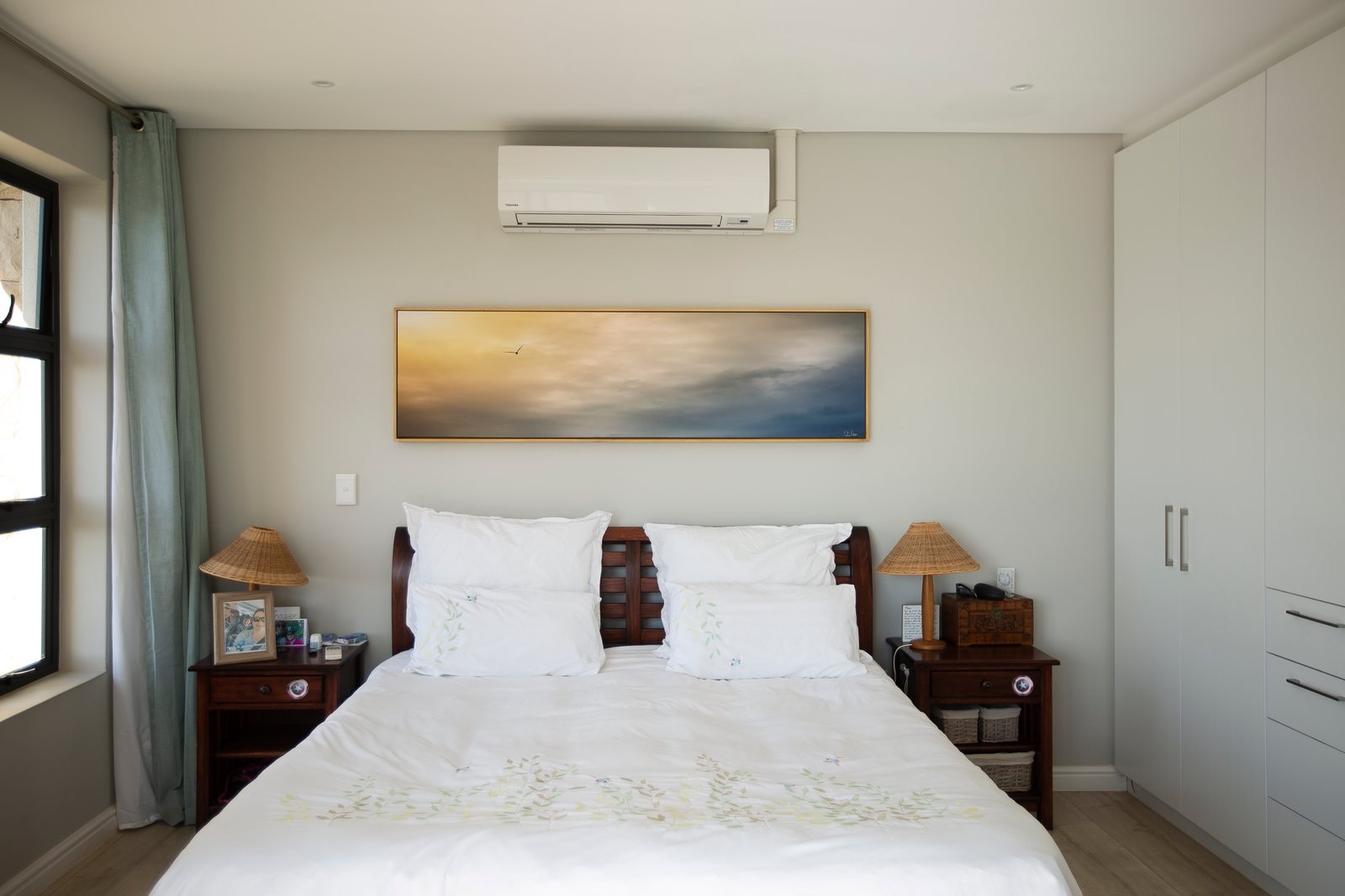 A long panoramic artwork above the bed in a calm neutral bedroom