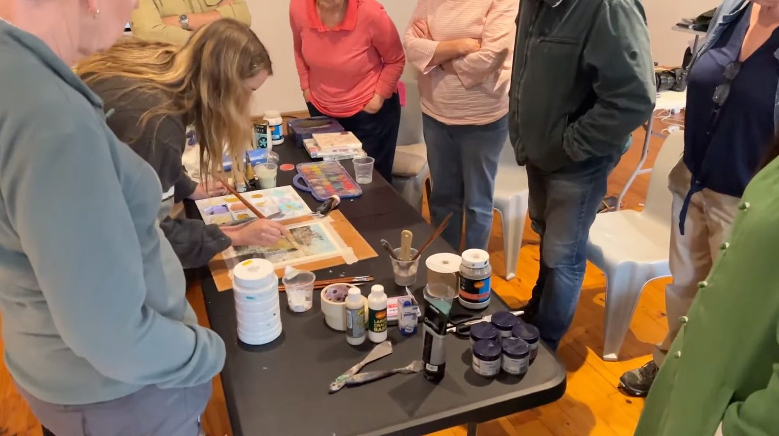 Samantha Lee Osner painting at the studio table while a group watches